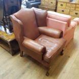 A brown leather wing back armchair, on cabriole legs