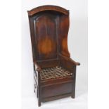 A late 18th/early 19th century country made oak lambing chair, with a panel and hooded back, the