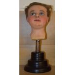 A 19th century wax head, with glass eyes, on an ebonised stand, 40 cm high