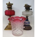 An early 20th century oil lamp with a cranberry glass shade, and various other oil lamps and