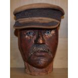 An early 20th century carved wooden head, with glass eyes, and a leather cap, 28 cm high