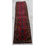 A Persian Hamadan woollen hand knotted runner with central medallions within borders on a red