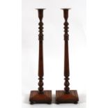 A pair of tall oak candlesticks with turned columns on square bases with bun feet, 59cms (23ins)