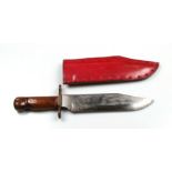 A large Bowie knife having hardwood grips and a brass crosspiece in its leather scabbard. No