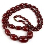 A string of graduated cherry amber Bakelite beads, the largest bead 3cms long, total weight 62g.