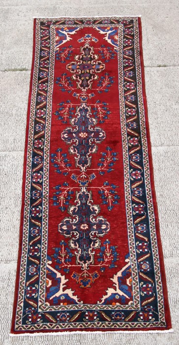 A Persian Hamadan woollen hand knotted runner with repeat foliate guls on a red ground, 283 by 98cms