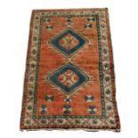 A Turkish Anatolian rug with two central guls within a stylised border on an orange ground, 189 by