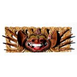 A painted and gilded carved wooden Thai mask wall plaque, 51cm (20ins) wide.