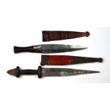 Two African tribal daggers in leather sheaths. Blade lengths of 22.5cms (8.875ins) and 17.5cms (6.