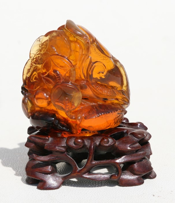 A carved amber group depicting fish amongst water foliage, on an associated pierced hardwood