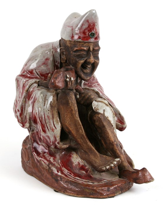 A Chinese Shiwan pottery figure in the form of an emaciated robed figure holding his shoe, impressed