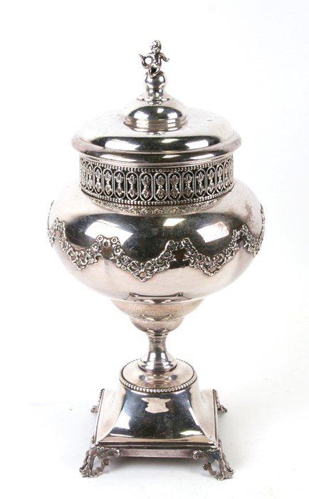 A continental silver plated jar and cover on stand with bow and foliate swag decoration, with cherub