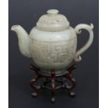 A Chinese jade or green hardstone tea pot, 12cms (4.75ins) high, on a five legged hardwood stand.