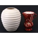 An Art Deco red glazed jug, 20cms (8ins) high; together with a white ribbed vase, 26cms (10ins) high