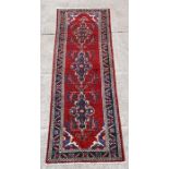 A Persian Hamadan woollen hand knotted runner with repeat foliate guls on a red ground, 283 by 98cms