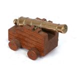 A desk top brass barrelled cannon mounted on a wooden carriage with wood wheels. Barrel length 13cms
