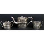 A Chinese white metal three-piece tea set comprising a teapot, sugar bowl and milk jug, decorated