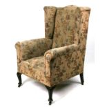 An upholstered wing back armchair on cabriole front supports.