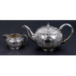 A Victorian silver teapot of compressed circular form decorated with scrolling foliage,