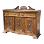 An Edwardian oak sideboard with two frieze drawers above three carved panelled doors, on a plinth