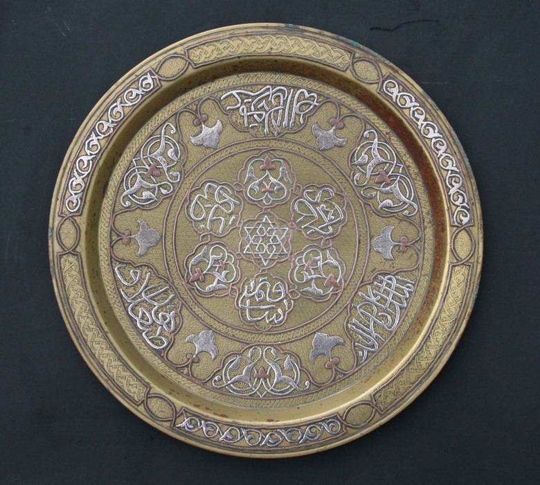 An Islamic bronze charger with silver and copper overlay including script and stylised foliate