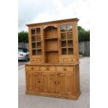 A pine dresser, the top section fitted with two glazed cabinets with shelving between, above three