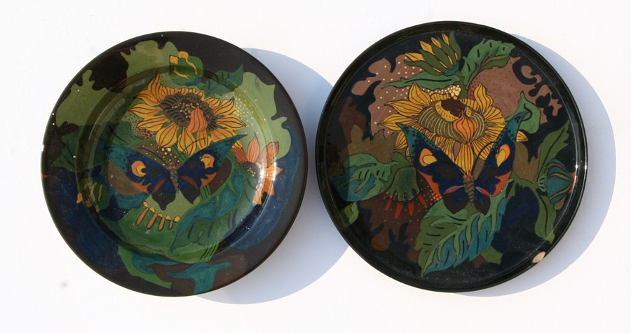 A Gouda pottery plate decorated with a butterfly and sunflowers; together with a similar shallow