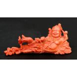 A Chinese pink coral figure depicting a recumbent Buddha with children playing on him, 11cms (4.