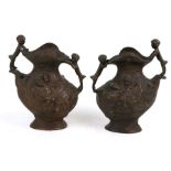 A pair of two-handled bronze vases decorated with children, 20cms (8ins) high.