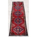 A Persian Azari runner with five geometric guls on a red ground, 297 by 101cms (117 by 40ins).