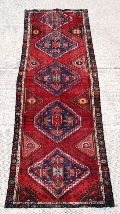 A Persian Azari runner with five geometric guls on a red ground, 297 by 101cms (117 by 40ins).