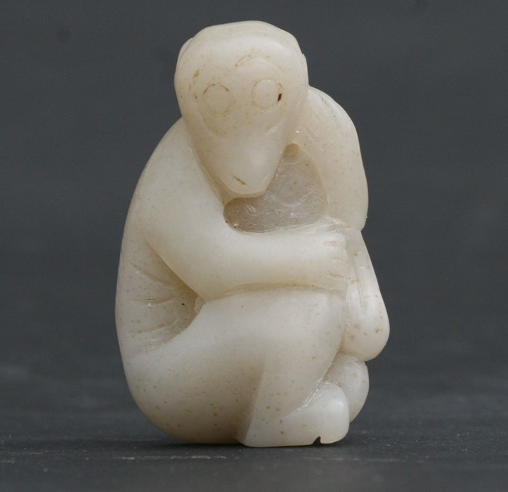 A Chinese mutton fat white jade figure carved in the form of a seated monkey, 5cms (2ins) high.