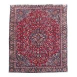 A Persian hand knotted woollen Mashad carpet on a red ground, 360 by 262cms (141.5 by 103ins).