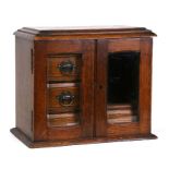 An oak smoker's cabinet with a pair of glazed doors enclosing shelves, 32cms (12.5ins) wide.