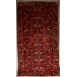 A Persian Hamadan hand knotted woollen runner with floral design within borders, on a red ground,