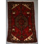 A Persian Hamadan hand knotted woollen rug with stylised central medallion within borders, on a