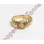 An 18 carat gold yellow sapphire and diamond ring, the oval cut with a diamond to each shoulder,