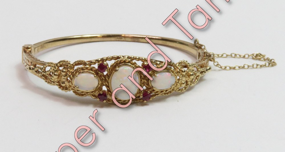 A 9 carat gold hinged bangle, set with three opals and four small ruby points, inner diameter