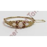 A 9 carat gold hinged bangle, set with three opals and four small ruby points, inner diameter