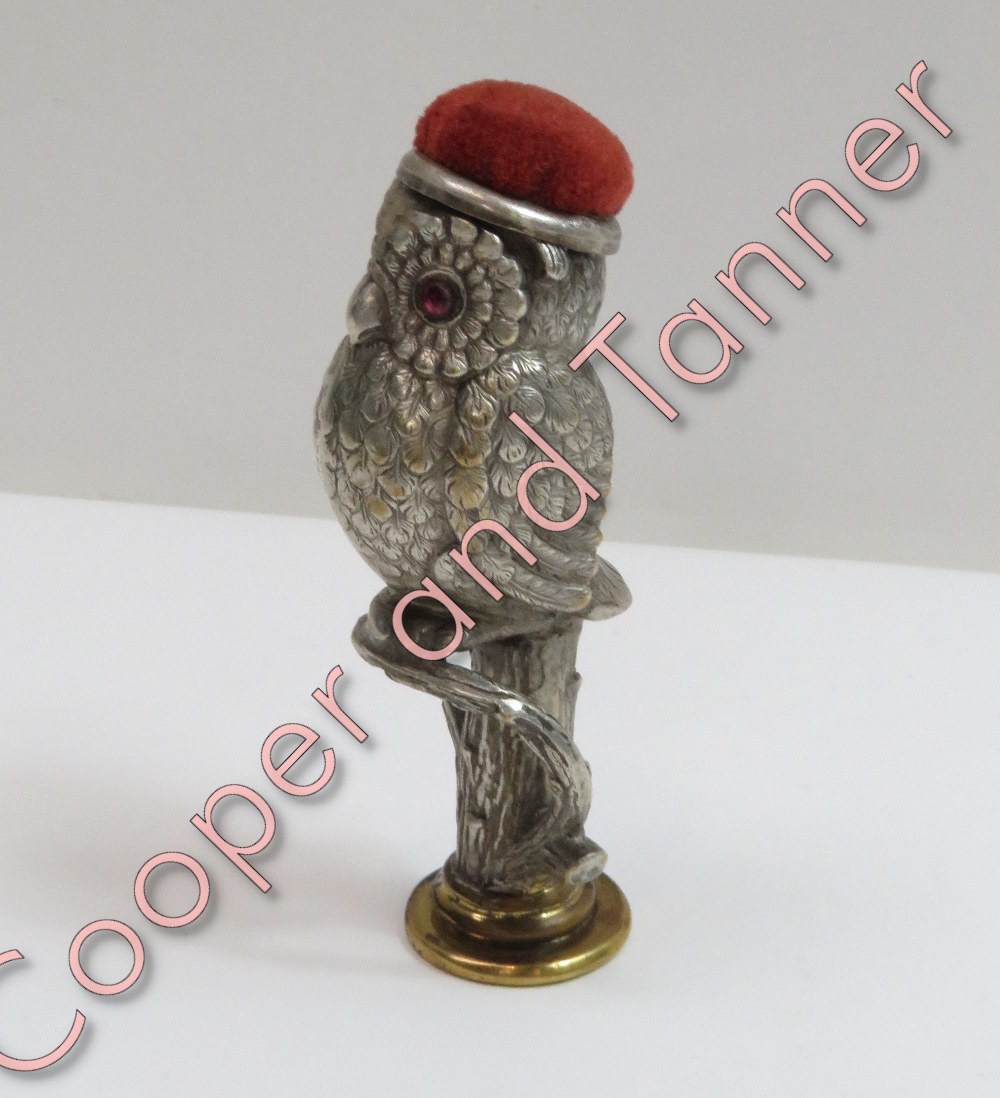 A metal pin cushion in the form of an owl on a tree stump, paste set eyes, monogrammed seal base,