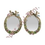 A pair of small Dresden style oval wall mirrors each surmounted by cherubs and with flower encrusted