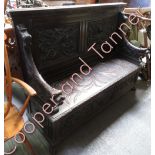 A carved oak bench seat the panelled back carved with mythical beasts, the arm rests with lion