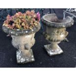 PAIR OF WEATHERED RECONSTITUTED STONE URN PLANTERS WITH CHERUB HEAD & FLORAL DECORATION