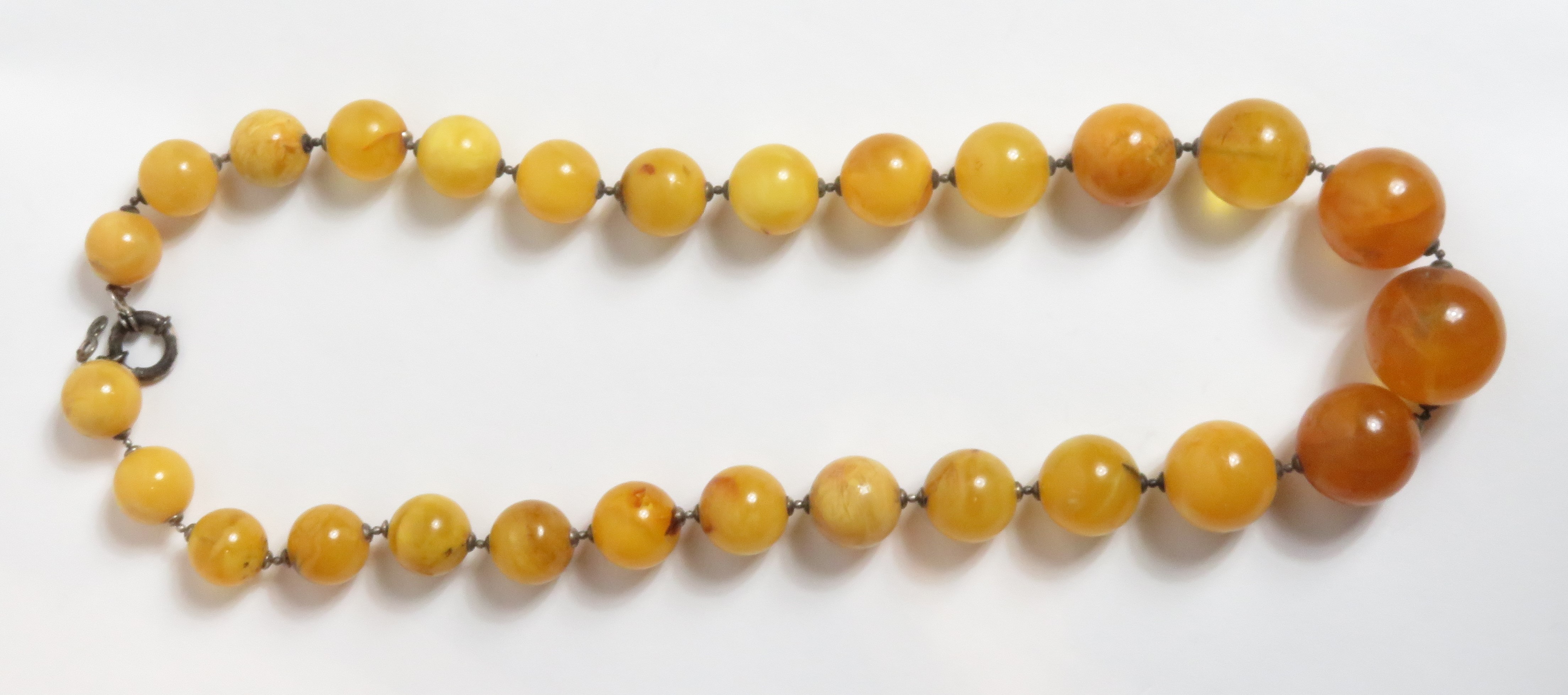 A graduated row of amber beads, the twenty seven round beads of approximately 1.5 cm - 2.5 cm