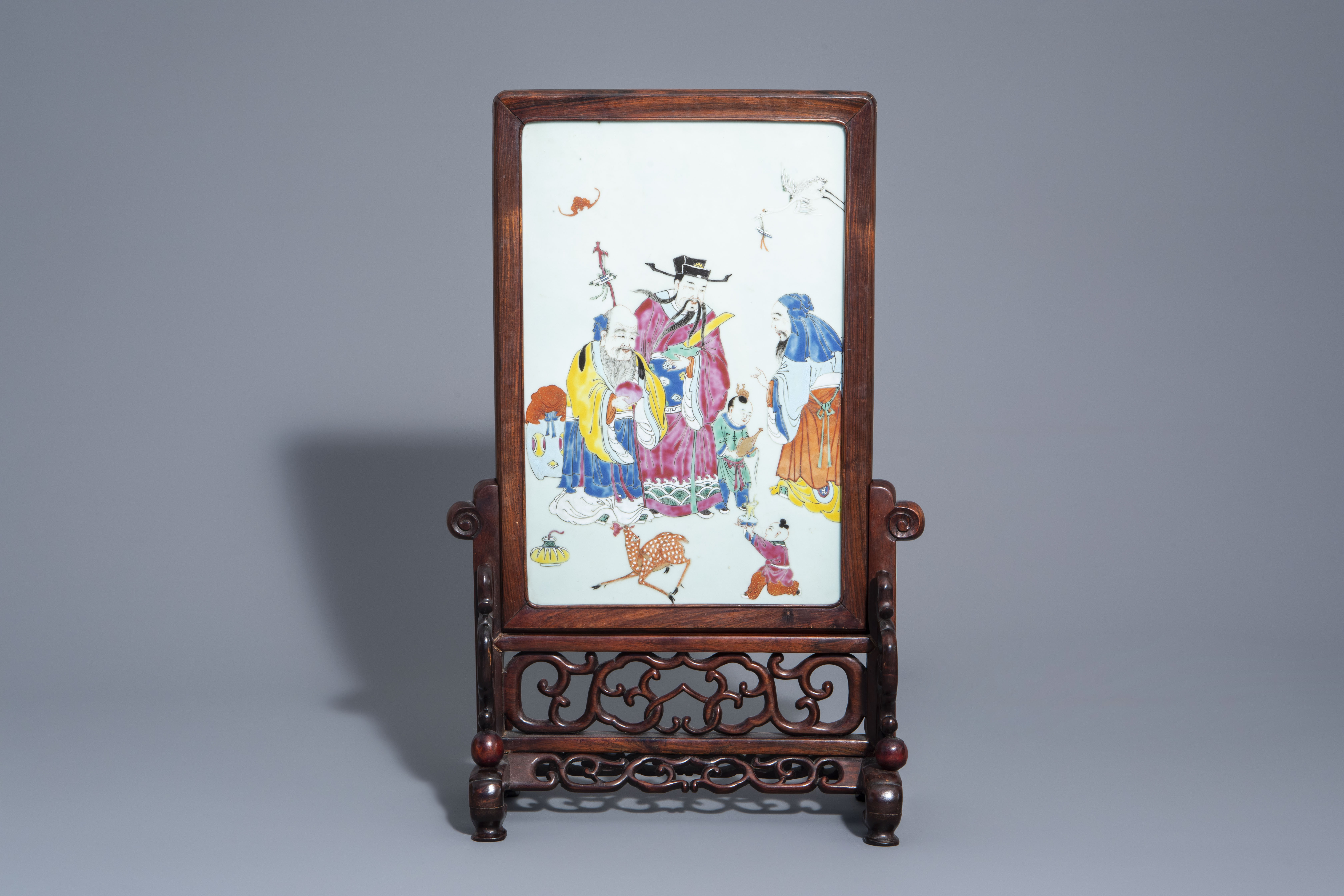 A Chinese wooden table screen with a famille rose plaque with the three star gods, 19th C.