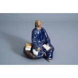 A Chinese Shiwan pottery figure of a man with a book, seal mark, Republic