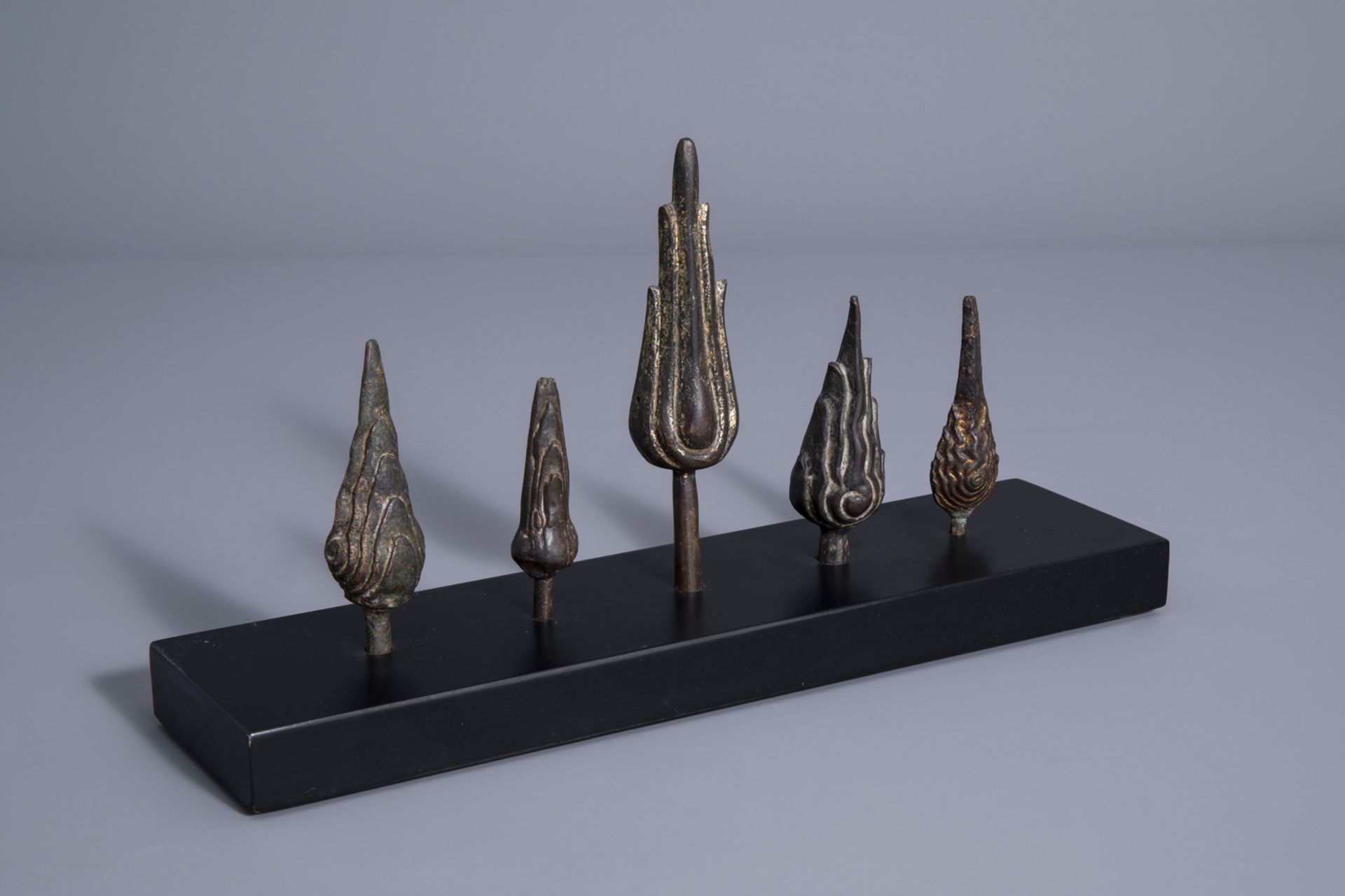 Five patinated and gilt bronze ushnishas on a wooden stand, Thailand/Cambodia, 19th/20th C.