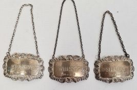 Three similar silver bottle labels marked 'Brandy', 'Sherry' and 'Whisky', with shell decoration