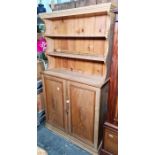 Probably early 20th century pine dresser with open shelves above two cupboard doors, plinth base,