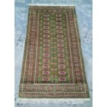 Green ground Persian rug with 28 elephant foot guls arranged across two rows, on a stepped border,